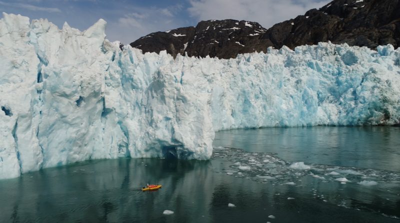 Green water and a huge wall of ice,and a tiny orange kayak.