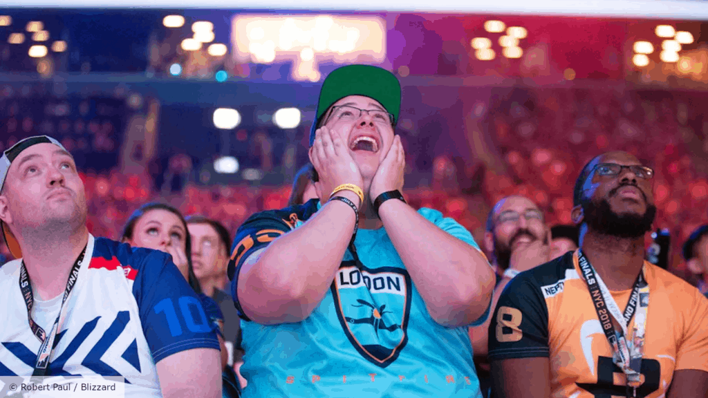 A close up of threew fans, one wearing a London Spitfire shirt, staring up at the stage during a live game.