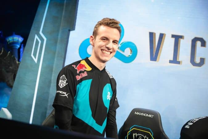 C9 LoL top laner Eric “Licorice” Ritchie stands up with a big grin in front of a monitor showing a C9 logo and the word victory