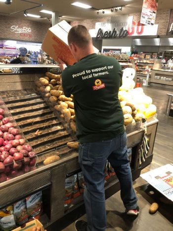 A Shop-Rite employee filling onion bins while wearing a shirt that says "proud to support our local farmers"