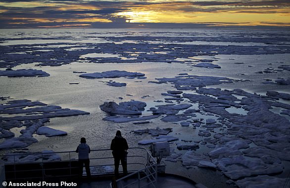 FILE - In this July 21, 2021 file photo, researchers look out from the Finnish icebreaker MSV Nordica as the sun sets over sea ice in the Victoria Strait along the Northwest Passage in the Canadian Arctic Archipelago. Studies show the Arctic is heating up twice as fast as the rest of the planet. Scientists are concerned because impacts of a warming Arctic may be felt elsewhere. (AP Photo/David Goldman, File)