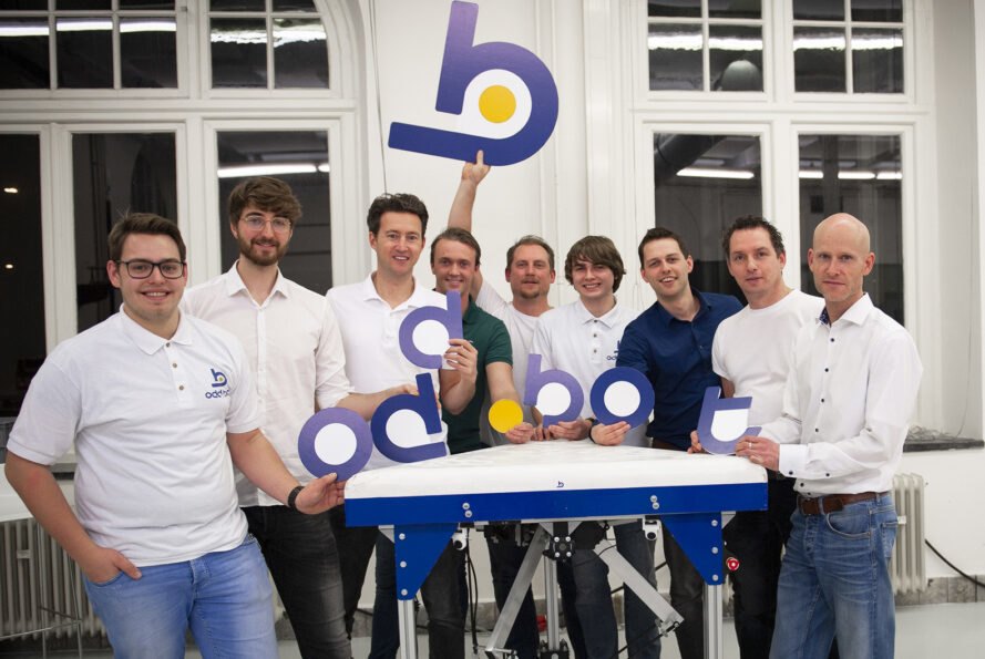 a group of people in white shirts (the Odd.Bot team), holding cutout letters that spell "Odd.Bot"