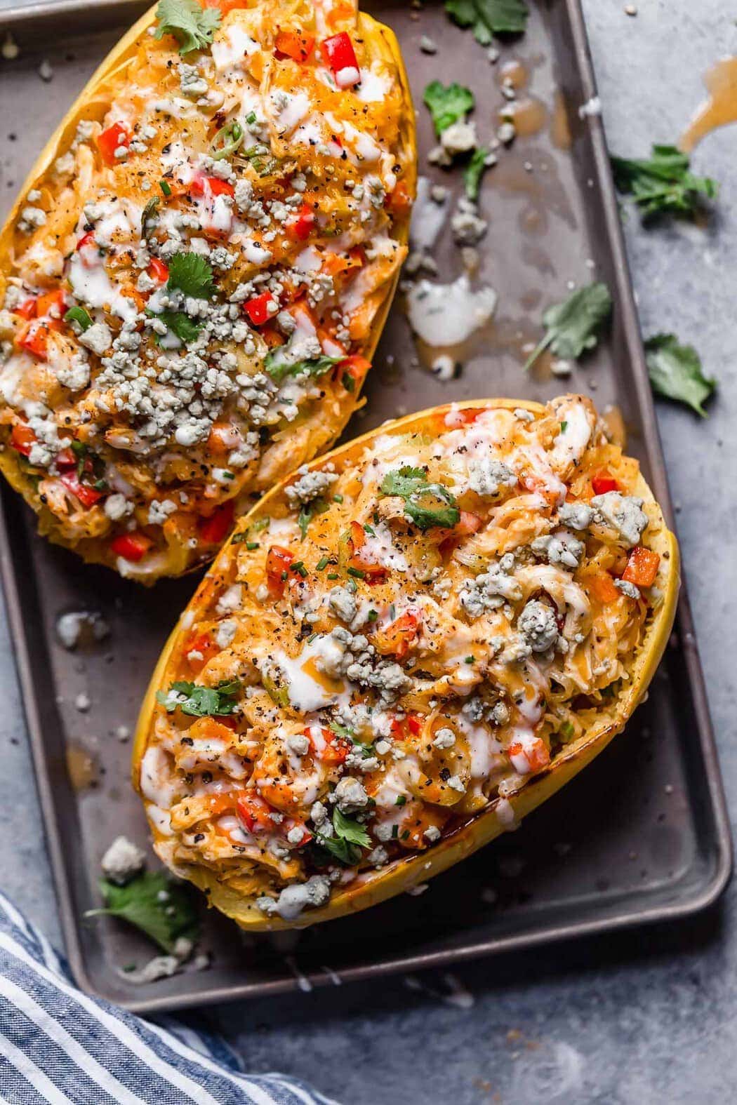 Two spaghetti squash halves stuffed with buffalo chicken, spaghetti squash and blue cheese crumbles on a sheet pan 