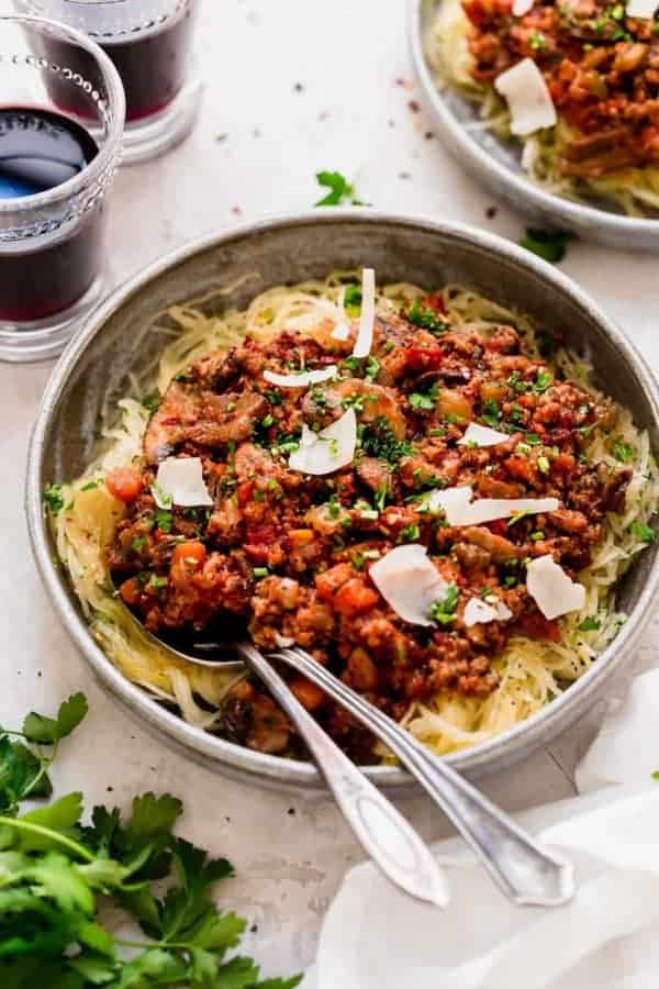 Bowl of turkey mushroom bolognese over noodles in a bowl with silverware in the bowl, two drinks in background