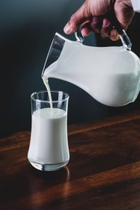Person pours milk from glass pitcher into glass